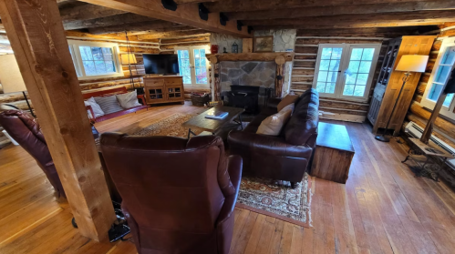 Cozy log cabin interior with wooden beams, a stone fireplace, and comfortable seating. Warm, inviting atmosphere.